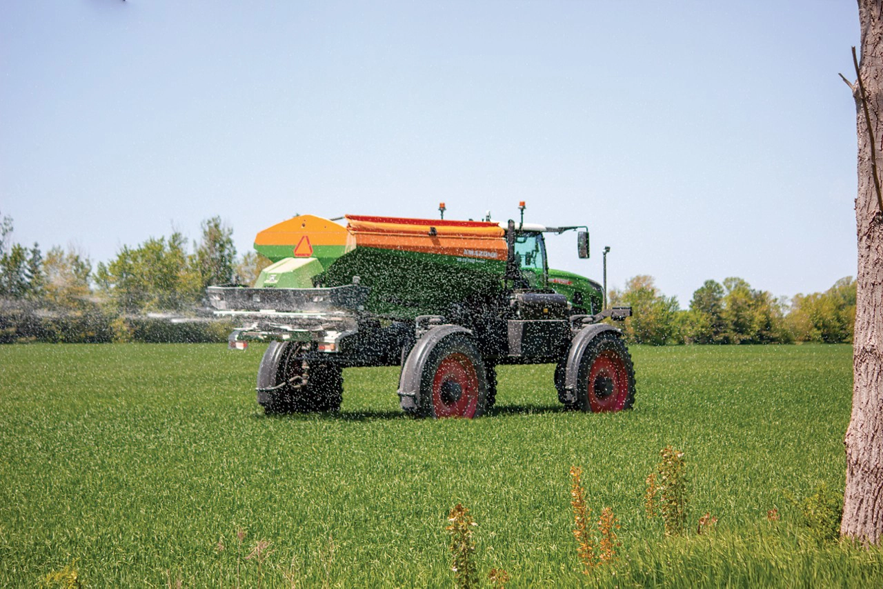 Fendt Rogator with an Amazone ZG-TS spreader actively distributing fertilizer in a green field, showcasing efficient coverage and precision agriculture technology.