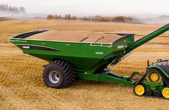 Brandt 1520XT grain cart filled with harvested grain in a golden field, attached to a track-equipped tractor for efficient offloading.
