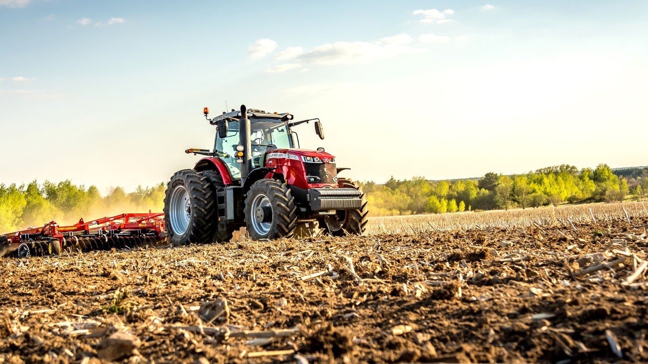 Massey Ferguson 8700S Series tractor pulling Sunflower tillage equipment across a harvested field during golden hour.