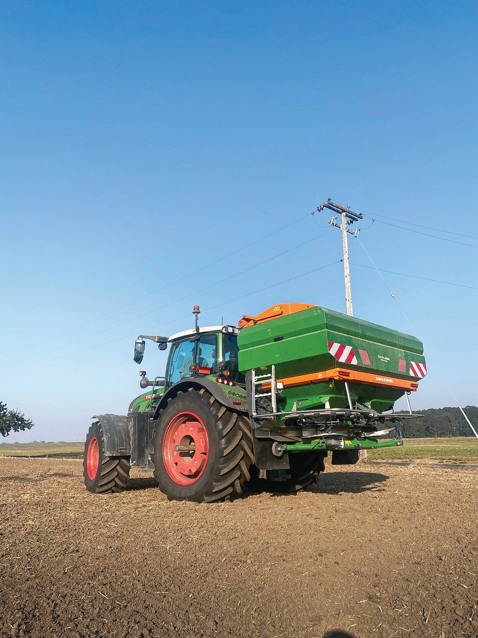 Fendt tractor with an Amazone ZA-TS fertilizer spreader parked on the side of a field.