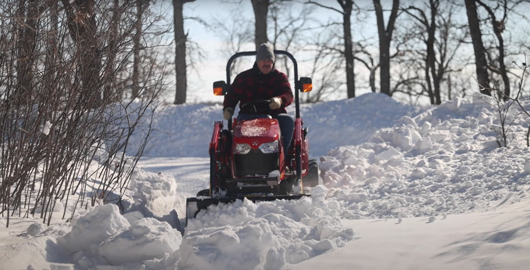 A Massey Ferguson GC1700 Series tractor clearing snow with a snow blade attachment on a residential driveway.