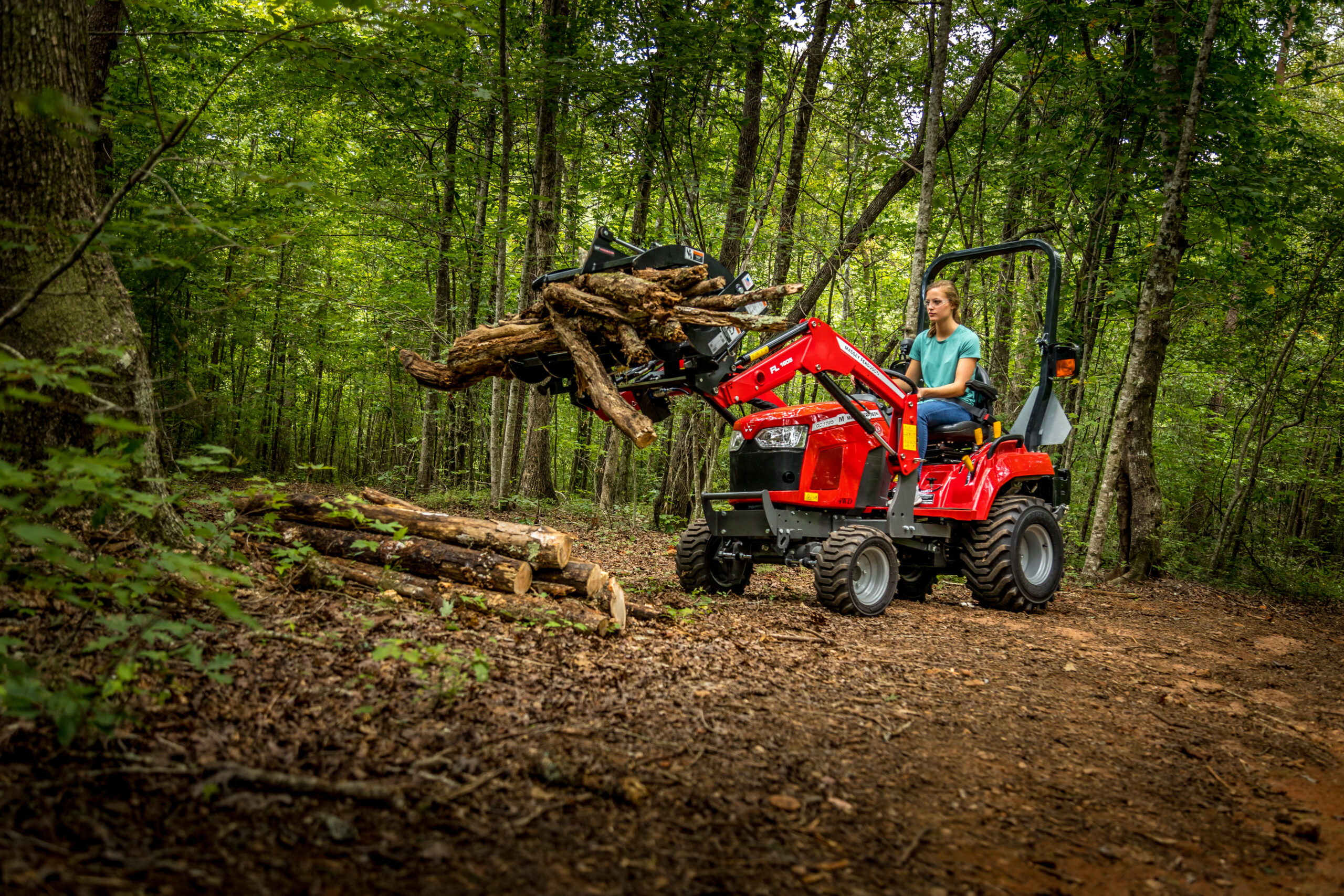 A Massey Ferguson GC1700 Series tractor with a front grapple attachment lifting logs, showcasing its high-capacity lifting power.