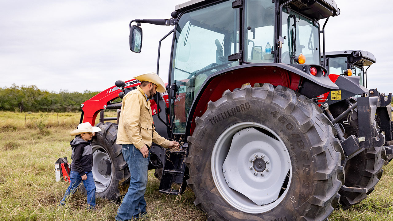 Farmer and child beside Massey Ferguson 5700 Series tractor, highlighting family farming and dependable AGCO equipment.
