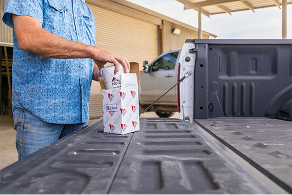 Man unloading an AGCO Parts package from the bed of a pickup truck outside a service facility.