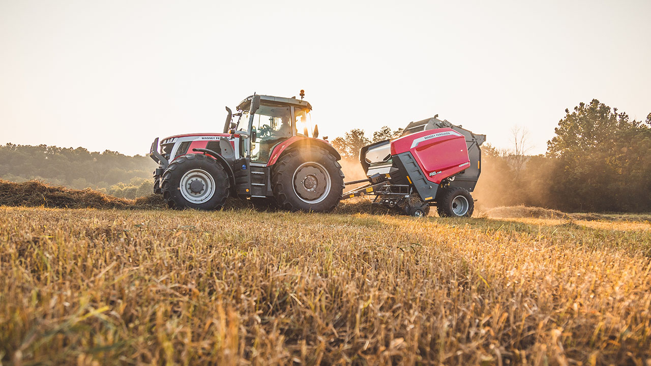 Hesston by Massey Ferguson 1 Series round baler working in a field at sunset with a Massey Ferguson tractor.