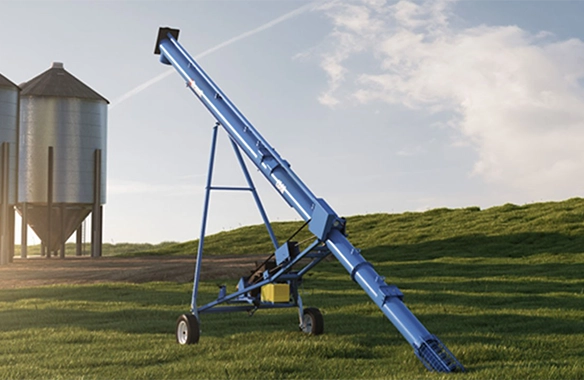Brandt portable grain auger positioned on a grassy hillside near silos, designed for efficient grain handling and transport on the farm.