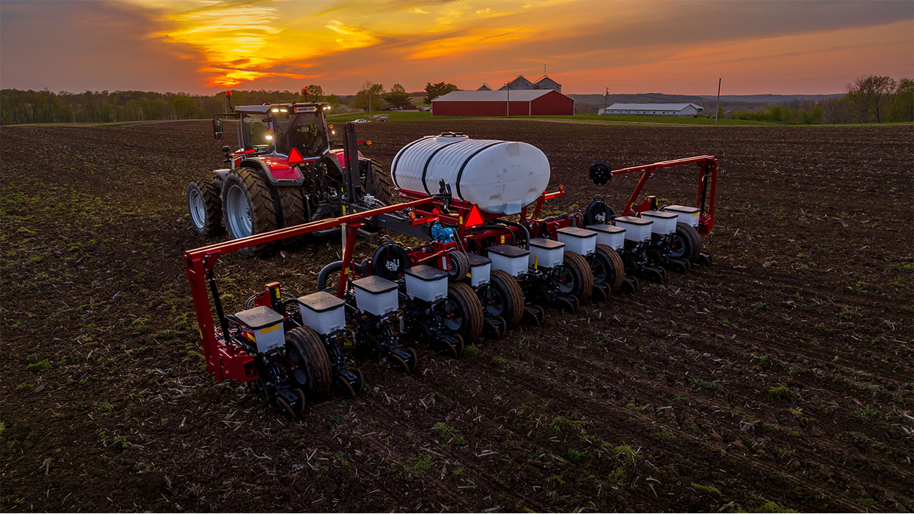 Rear view of a Massey Ferguson planter in action at sunset, planting rows across a field with precision AGCO farming technology.