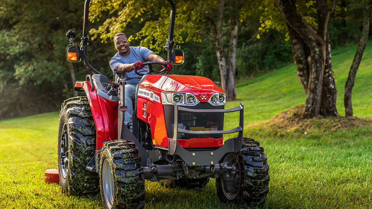 Smiling operator mowing lawn on a Massey Ferguson 1800M compact tractor, ideal for residential and property maintenance tasks.