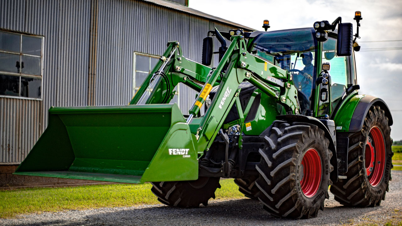 Fendt 300 Vario tractor with front loader parked on gravel near farm buildings, ready for versatile AGCO farm work.