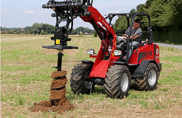 Schäffer 3650 compact loader using an auger attachment to drill a hole in a farm field for post or fence installation.