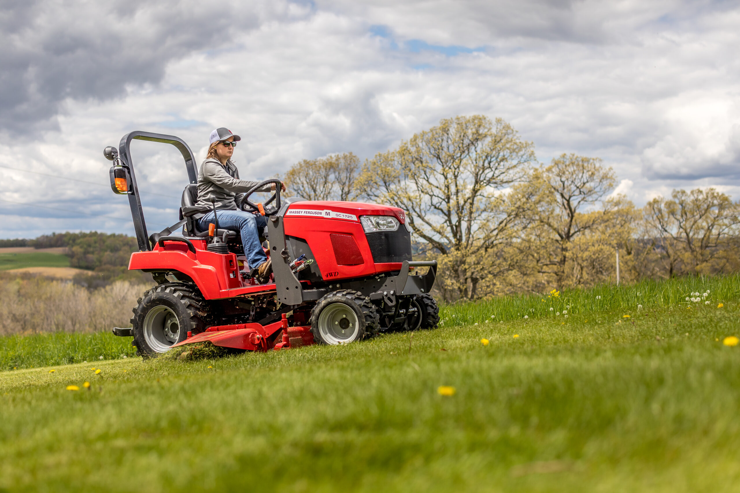 A Massey Ferguson GC1700 Series sub-compact tractor mowing a large field with a mid-mount mower attachment.
