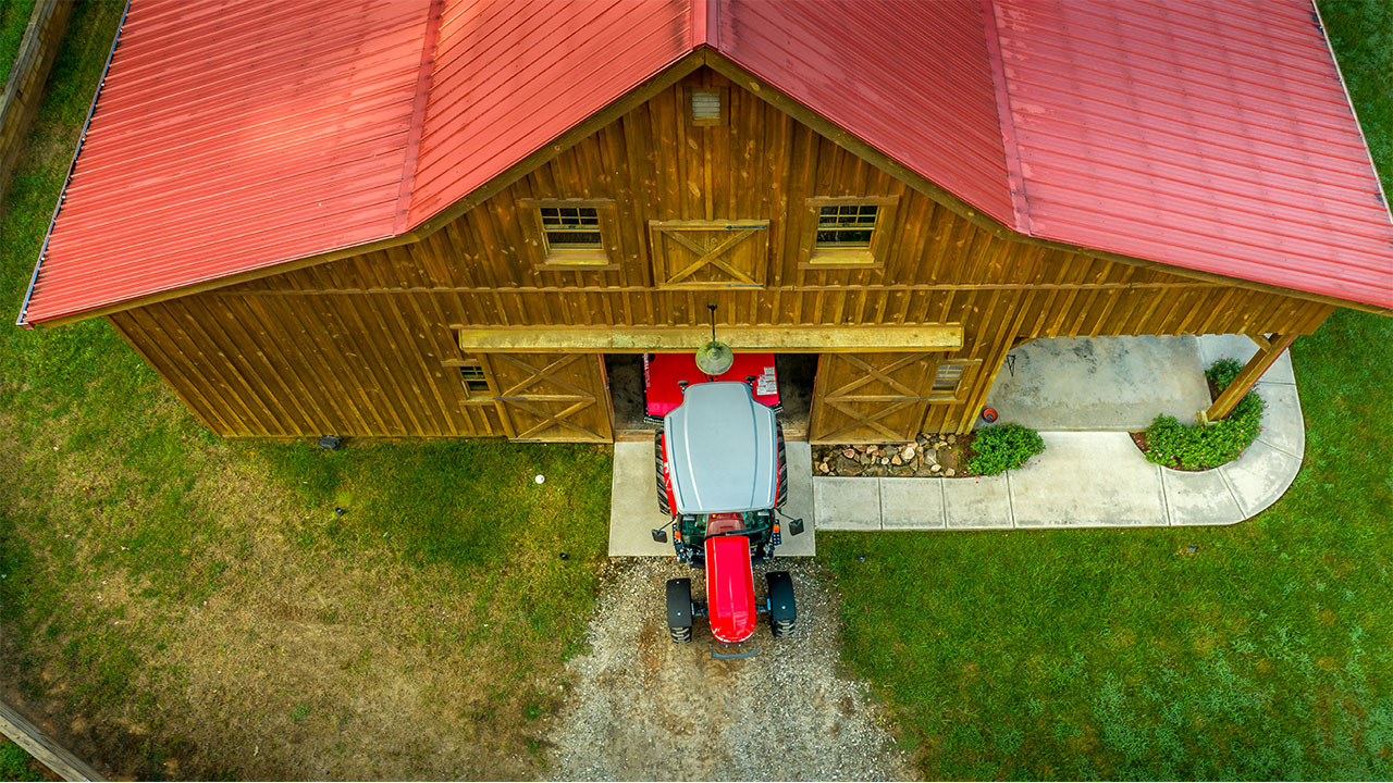 Top-down view of a Massey Ferguson 2800M tractor entering a red-roof barn, ideal for compact farms and rural property upkeep.