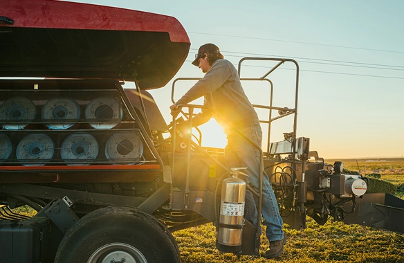 Operator inspecting Hesston by Massey Ferguson 1436 Series large square baler at sunrise, emphasizing maintenance accessibility and field-ready reliability for hay production.
