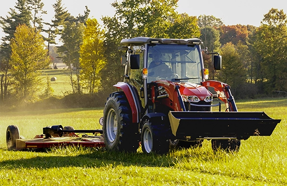 Massey Ferguson 2M Series compact utility tractor with front loader and rotary cutter mowing a large pasture, ideal for field maintenance and land management tasks.