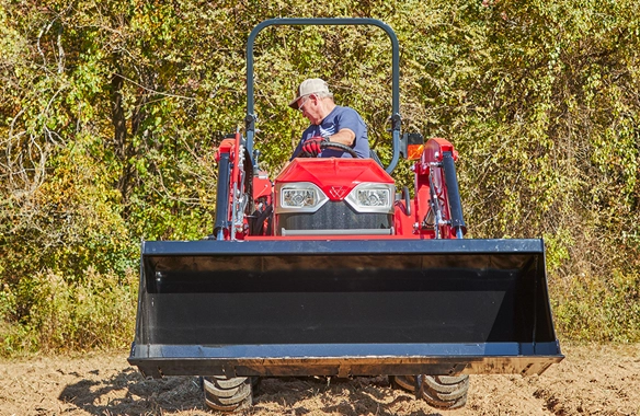 Front view of a Massey Ferguson 1E Series compact tractor with a front loader, operated by a man in a field, illustrating its strength and ease of control in outdoor environments.