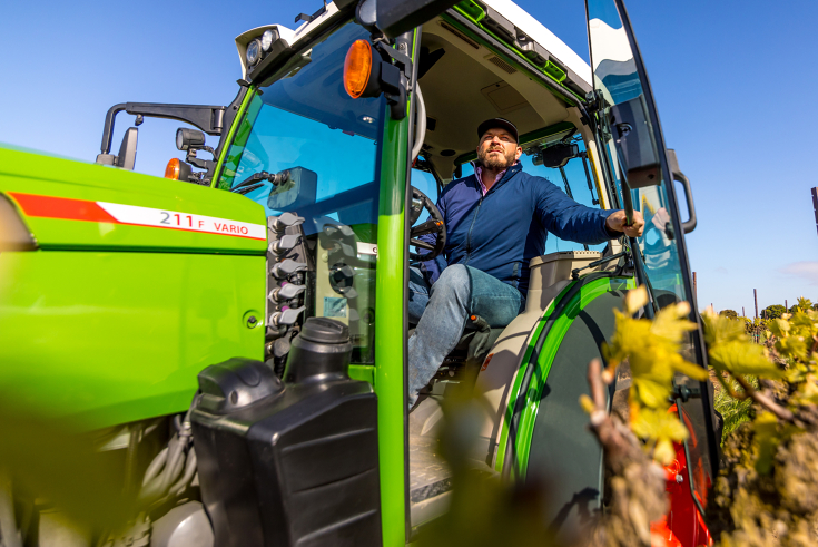 Farmer operating Fendt 211 F Vario tractor in vineyard, ideal for narrow-row specialty crops and orchard applications.