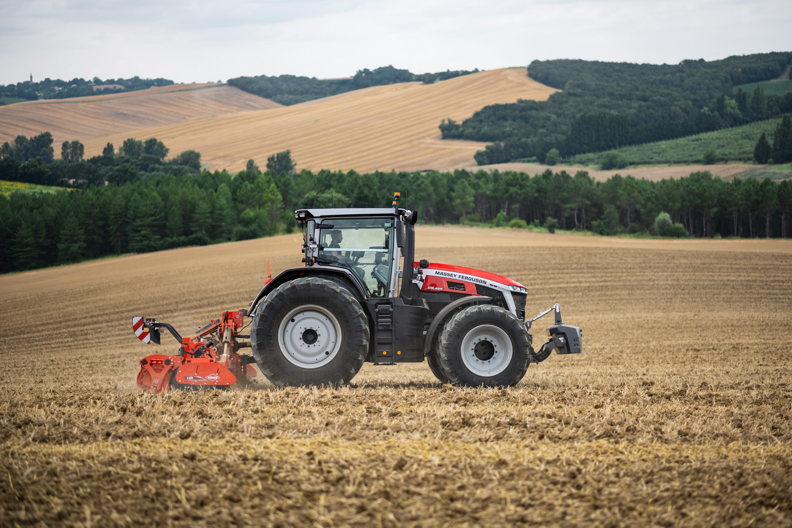 Massey Ferguson 9S Series tractor working in a harvested field with tillage equipment in rolling countryside terrain.