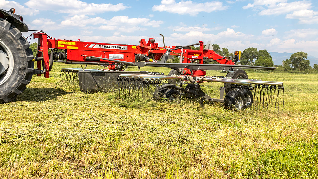 Massey Ferguson rotary rake in action, efficiently gathering hay for baling in a sunny field with clear skies.