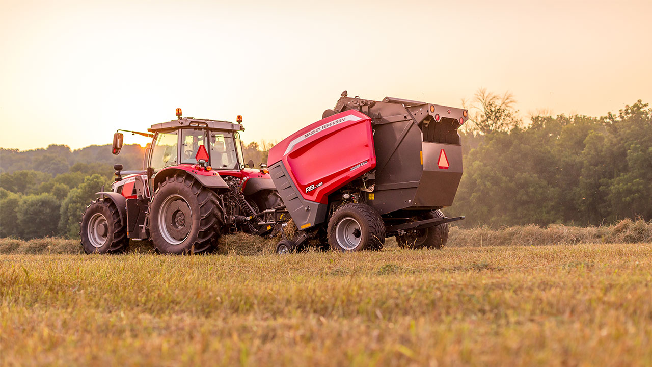 Hesston by Massey Ferguson 1 Series round baler in action with tractor during sunset harvest in a hay field.