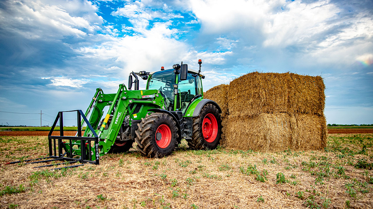 Fendt 300 Vario tractor with Fendt front loader stacking hay bales in a field, showcasing AGCO precision and power.