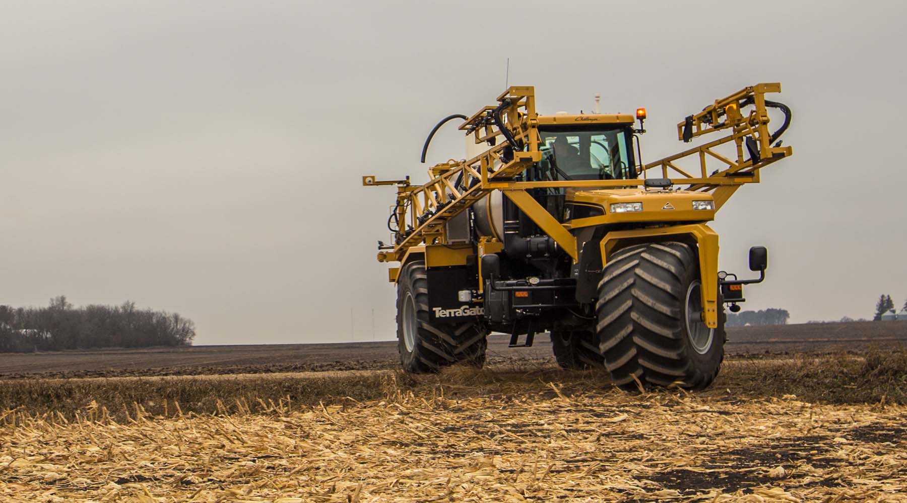 TerraGator C Series applicator with folded boom parked in corn stubble field under cloudy sky.