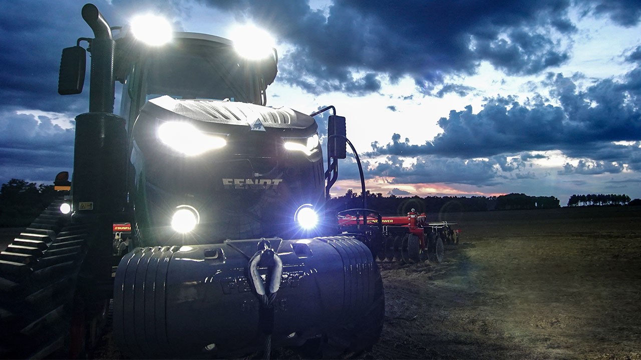 Fendt 900 Vario MT tractor with headlights on, working with Sunflower tillage tool at dusk in the field for high-efficiency farming.
