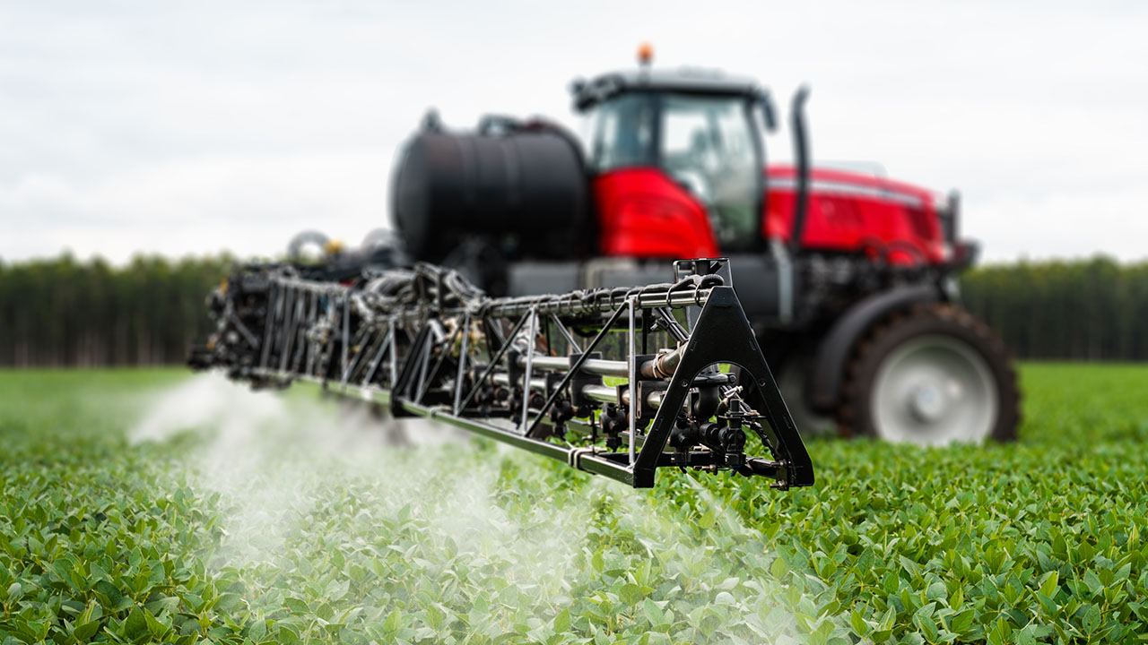 Close-up of Massey Ferguson sprayer boom applying chemicals over crops with precision in a green field.