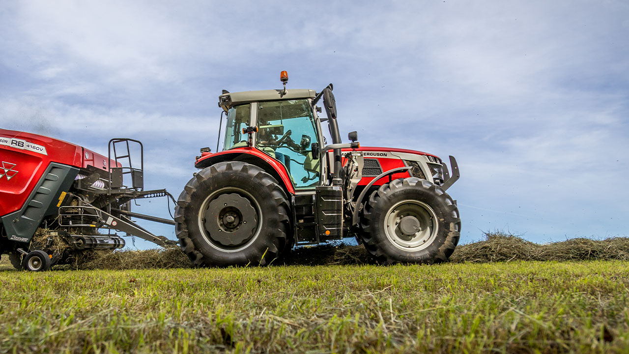 Massey Ferguson 6S Series tractor operating with RB 4160V round baler, producing hay bales in a green field under a clear sky.