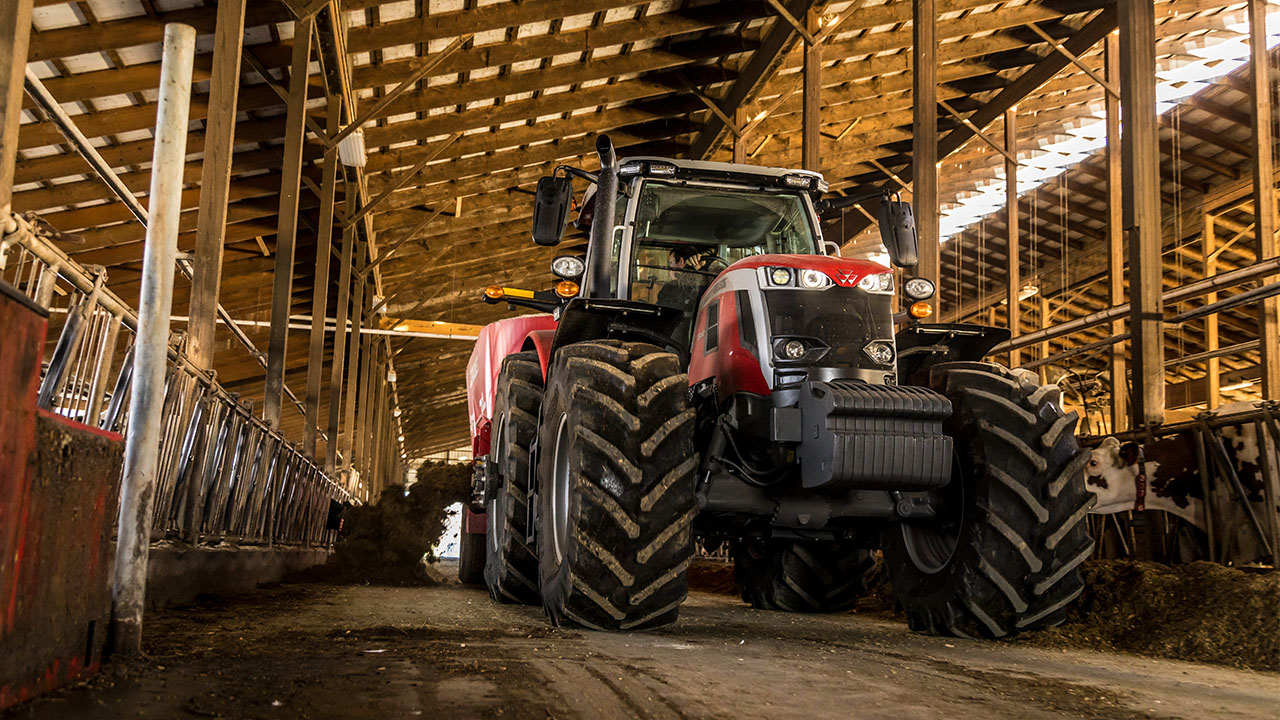 Massey Ferguson 7S Series tractor hauling a red feed mixer on a livestock farm.
