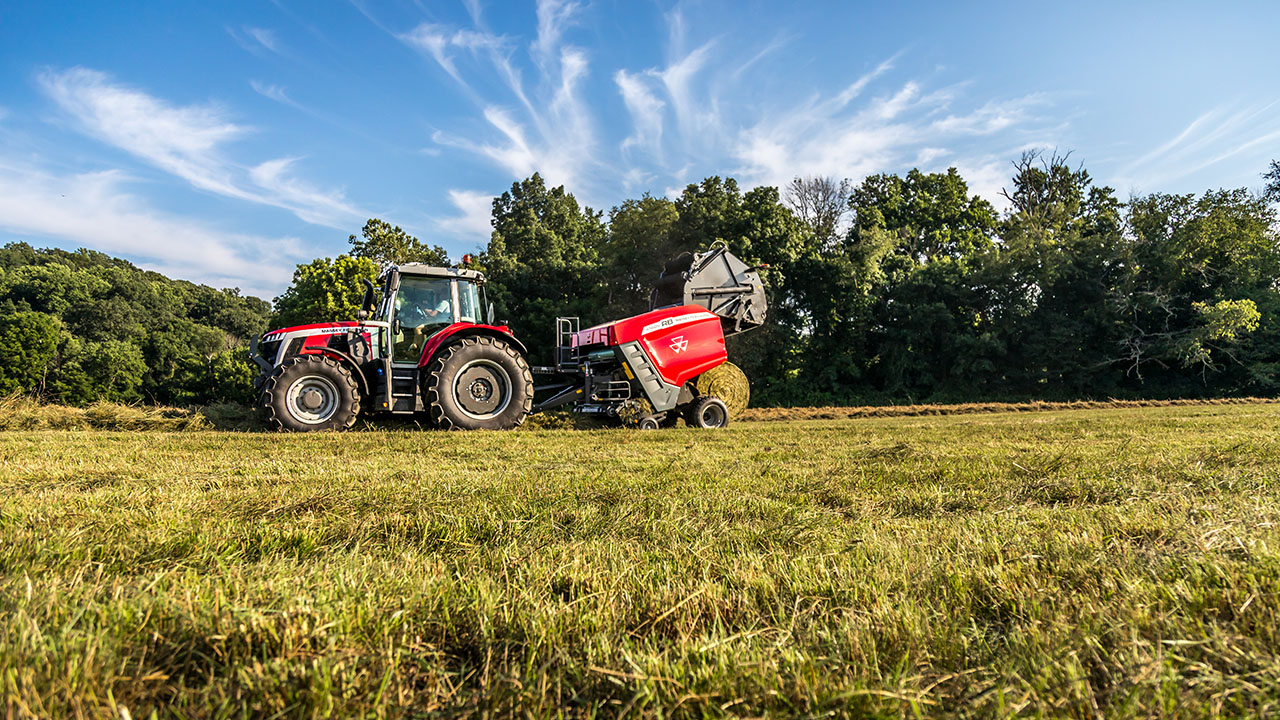 Hesston by Massey Ferguson RB Series round baler working in hayfield with MF tractor, producing dense round bales under blue sky.