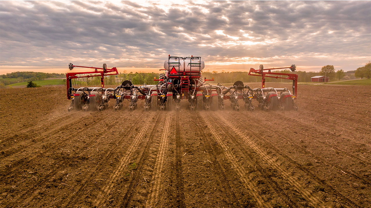 Rear view of a Massey Ferguson planter in action at sunrise, planting rows across a field with precision AGCO farming technology.