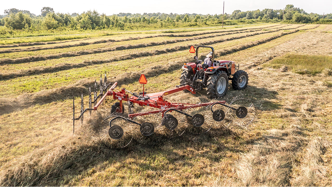 Massey Ferguson tractor using MF RK V Series Wheel Rake to form clean windrows in a large hayfield under sunny skies.